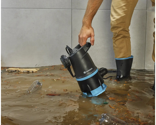 Eine Person benutzt eine Gardena Schmutzwasserpumpe in einem überfluteten Raum.