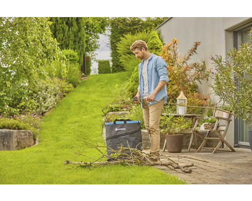 Mann schneidet Gartenabfälle mit einer Gartenschere und einem Gartensack im Garten.
