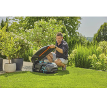 Mann öffnet den Deckel eines Rasenmähroboters auf einem Rasen