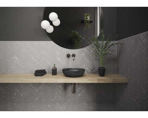 Modernes Badezimmer mit Waschtisch, Spiegel, Lampe und grauen Fliesen in Fischgrätmuster.