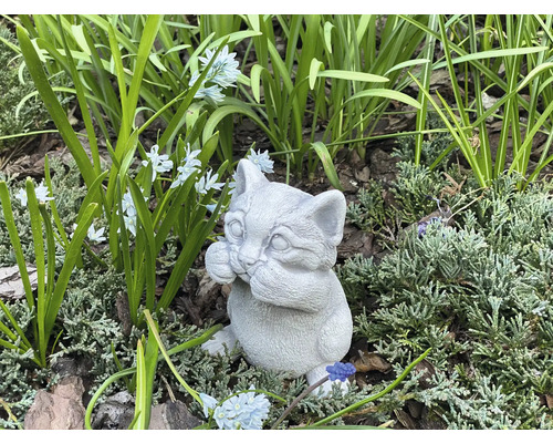 Dekorative Katzenfigur aus Stein für den Garten zwischen Pflanzen und Blumen