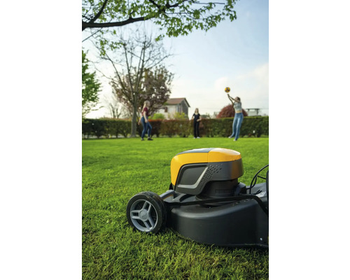 Rasenmäher auf Rasen mit spielenden Personen im Hintergrund