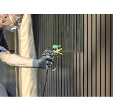 Person lackiert Zaun mit Farbsprühgerät