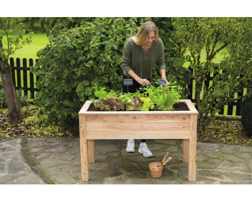 Frau gärtnert in einem Hochbeet aus Holz im Garten.