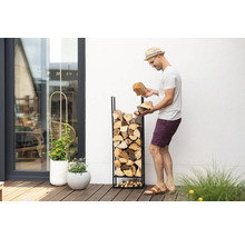 Mann befüllt ein Brennholzregal mit Holzscheiten im Garten