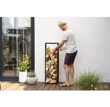 Mann befüllt Brennholzregal mit Holz auf einer Terrasse
