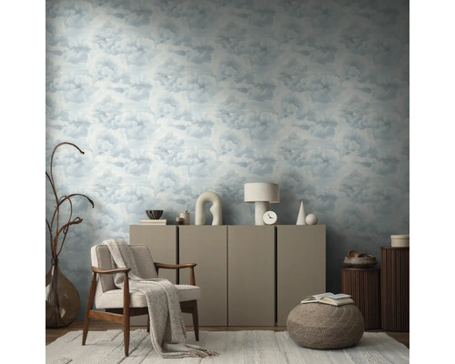 Wohnzimmer mit Wolkenmuster-Tapete, Sessel, Kommode und dekorativen Elementen für eine wohnliche Atmosphäre