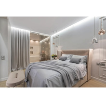 Helles Schlafzimmer mit Doppelbett, Nachttisch und angrenzendem Badezimmer hinter einer Glasschiebetür