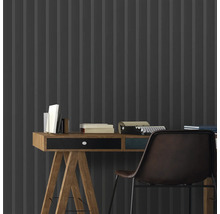 Nahaufnahme eines Schreibtisches mit Büchern und einer Schreibmaschine vor einer grauen Wandtapete mit Streifenmuster.