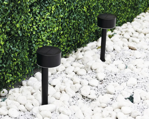 Zwei schwarze Solarleuchten im Garten zwischen weißen Steinen und einer grünen Hecke