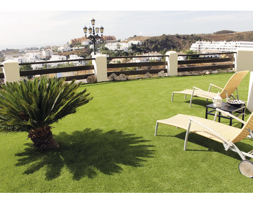 Szene mit Kunstrasen, Sonnenliegen und einem kleinen Baum auf einem Balkon mit Blick auf eine Stadt.