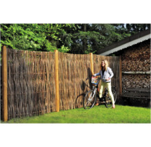 Gartenszene mit einem Zaun aus Naturmaterialien und einer Frau mit Fahrrad