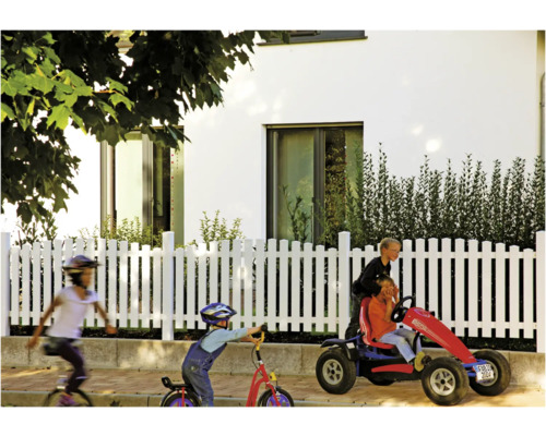 Szene mit Kindern, die mit einem Einrad, einem Tretroller und einem Pedal Go-Kart vor einem Haus mit weißem Zaun spielen.