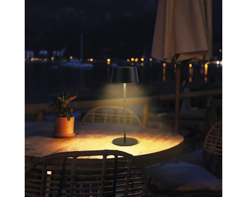 Außenaufnahme einer Tischleuchte auf einem Holztisch im Freien bei Nacht.