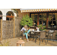 Terrasse mit Sichtschutzzaun, Gartenmöbeln und lesender Frau.