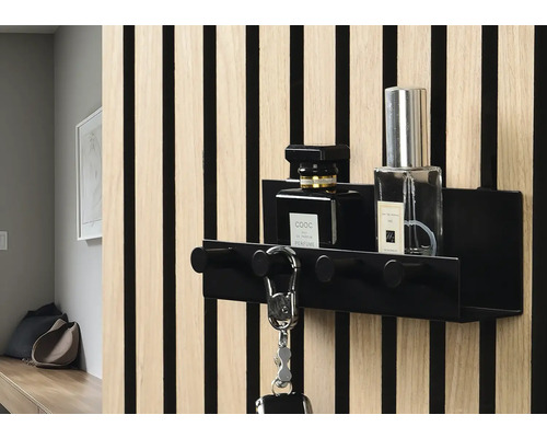 Schwarze Schlüsselablage mit Haken und zwei Parfümflaschen an einer Wand mit Holzverkleidung