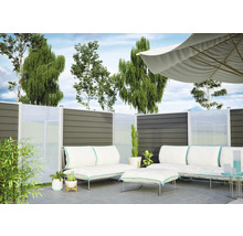 Modernes Garten-Lounge-Set mit weißen Polstern und Sonnenschirm vor einem Sichtschutzzaun aus grauen Paneelen und Glas auf einer Terrasse.