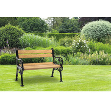 Gartenbank aus Holz und Metall auf Rasen vor üppiger Gartenlandschaft