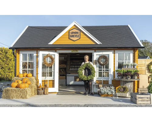 Ein gelbes Gartenhaus mit einer Frau, die einen Kranz hält und Kürbisse davor.