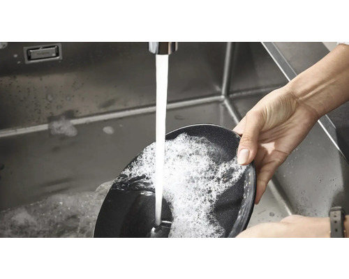 Eine Person spült eine Bratpfanne in einem Spülbecken unter fließendem Wasser.