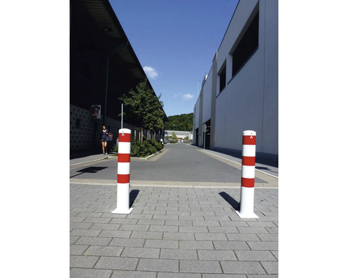 Zwei rot-weiß gestreifte Absperrpfosten auf einem gepflasterten Weg.