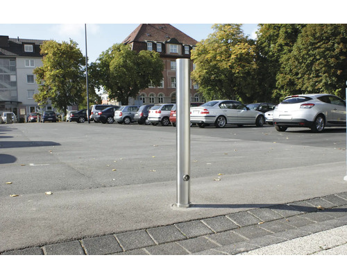 Versenkbarer Poller aus Metall auf einem Parkplatz mit geparkten Autos.