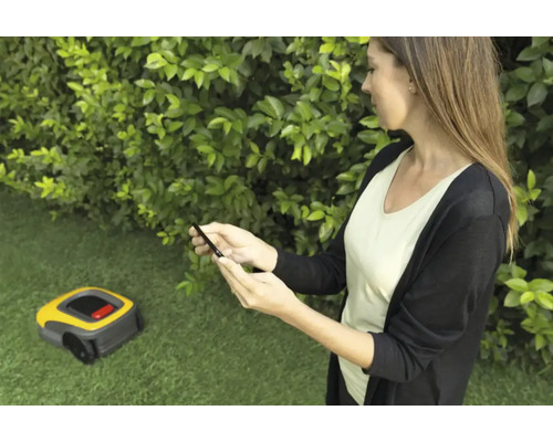Frau bedient Rasenmähroboter mit Smartphone im Garten.
