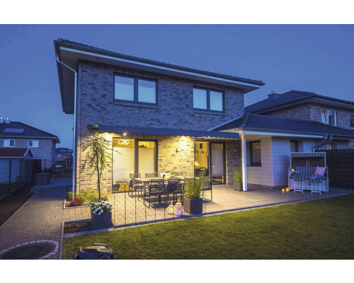 Beleuchtete Terrasse mit Markise, Tisch, Stühlen und Rasenmähroboter im Garten.