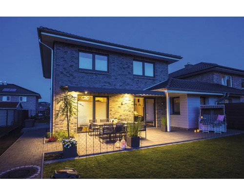 Haus mit Terrasse, Gartenmöbeln, Markise und Rasenmähroboter bei Dämmerung