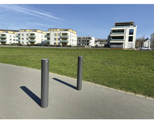 Zwei Poller aus Metall auf einem Bürgersteig mit Wohnhäusern im Hintergrund
