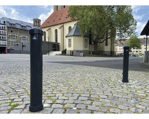 Zwei runde Absperrpfosten auf einem gepflasterten Platz vor einem Gebäude