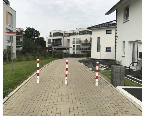 Pfosten auf einem gepflasterten Weg vor Wohngebäuden.