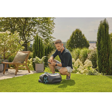 Mann bedient Rasenmähroboter mit dem Smartphone im Garten