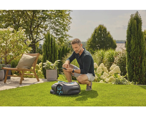Mann bedient Rasenmähroboter mit dem Smartphone im Garten
