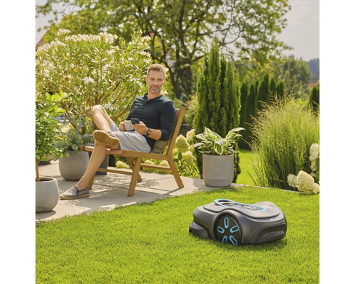 Ein Mann entspannt im Garten mit einem Rasenmähroboter im Vordergrund