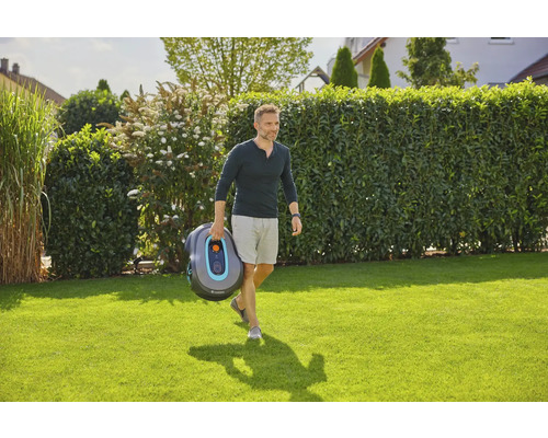Mann trägt Gardena Mähroboter im Garten