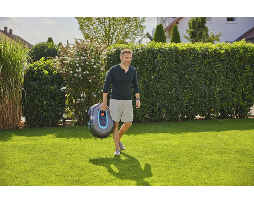 Mann trägt Gardena Mähroboter über Rasen