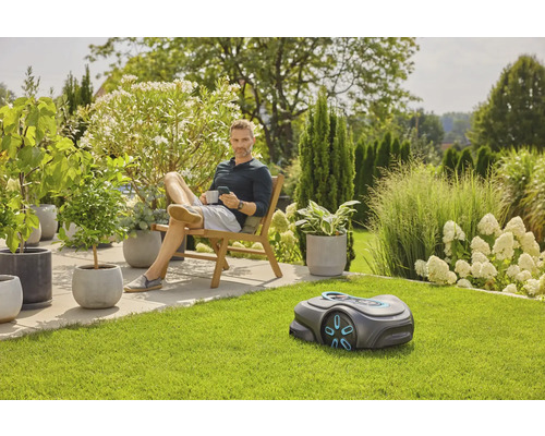 Mann entspannt im Garten mit Rasenmähroboter, Pflanzen und Gartenmöbeln