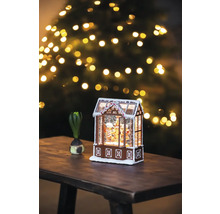 Dekoratives Lebkuchenhaus mit Schnee und Weihnachtsbaum im Hintergrund