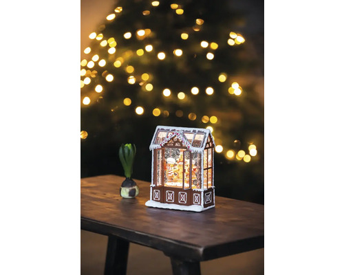 Dekoratives Lebkuchenhaus mit Schnee und Weihnachtsbaum im Hintergrund