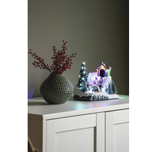 Dekorative Winterlandschaft mit Haus, Tannenbaum und Schlittschuhläufern neben einer Vase mit roten Beeren auf einem Schrank