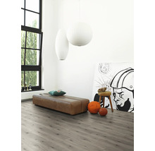 Heller Raum mit grauem Laminatboden, brauner Sitzbank, Kunstwerk und großen Fenstern für eine freundliche Atmosphäre