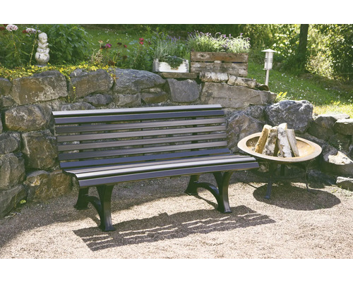 Eine Gartenbank aus Holz und Metall steht im Garten neben einer Feuerstelle.