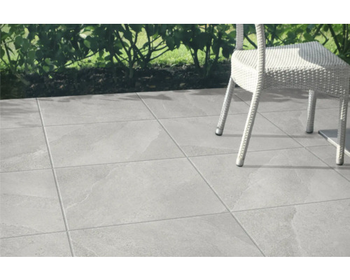 Verlegte graue Terrassenfliesen mit Gartenstuhl