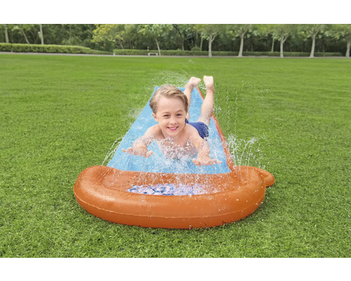 Junge rutscht auf einer aufblasbaren Wasserrutsche im Garten