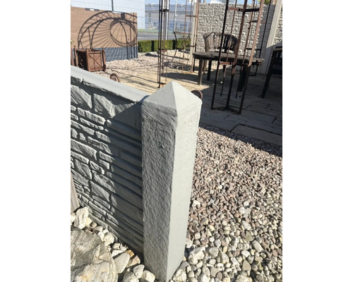 Betonzaunpfosten mit pyramidenförmiger Spitze in einem Gartenbereich.