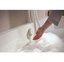 Hand prüft das Wasser aus einem Unterputz-Badewannenarmatur in einer mit Schaum gefüllten Badewanne