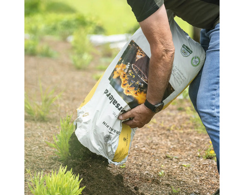 Eine Person schüttet Blumenerde aus einem Sack auf ein Beet.