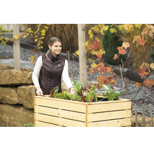 Frau mit Gartenwerkzeug an einem Hochbeet mit Gemüse.