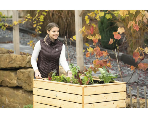 Frau mit Gartenwerkzeug an einem Hochbeet mit Gemüse.